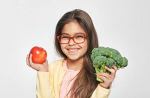 Smiling mixed race girl holding an apple and broccoli in her hands. Healthy vegetarian food for kids, nutrition