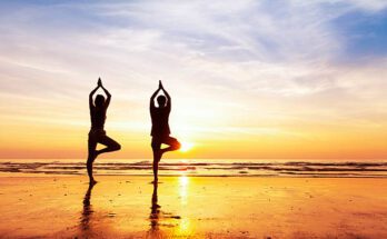 Two people practicing yoga tree position on the beach with beautiful sunset and reflection